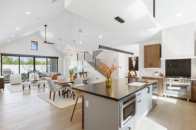 kitchen featuring high vaulted ceiling, sink, an island with sink, appliances with stainless steel finishes, and decorative light fixtures