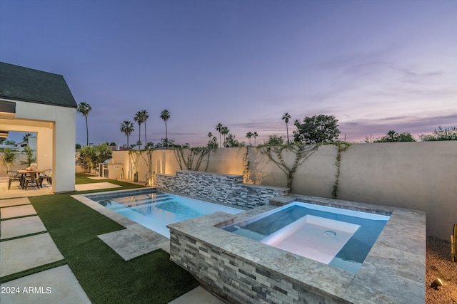 pool at dusk with a patio area and an in ground hot tub