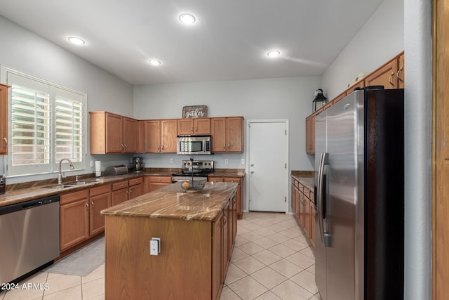 kitchen with stainless steel appliances, a center island, light tile patterned floors, sink, and dark stone countertops