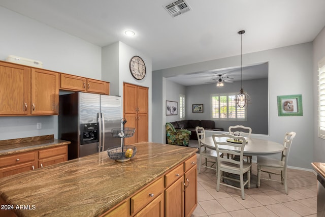 kitchen featuring hanging light fixtures, light tile patterned flooring, ceiling fan, dark stone countertops, and stainless steel fridge