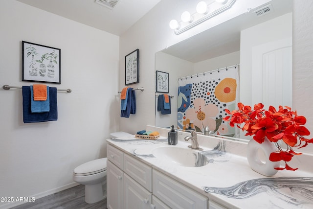 bathroom featuring visible vents, wood finished floors, vanity, baseboards, and toilet