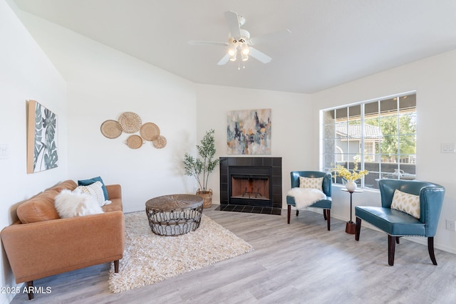 living area with a tiled fireplace, baseboards, a ceiling fan, and wood finished floors
