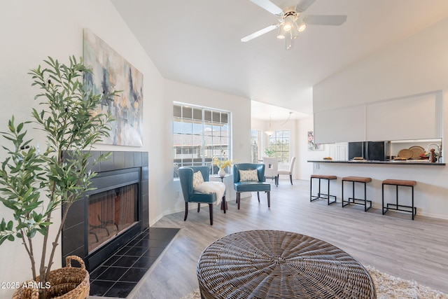 living area featuring a ceiling fan, a fireplace, light wood-type flooring, baseboards, and lofted ceiling