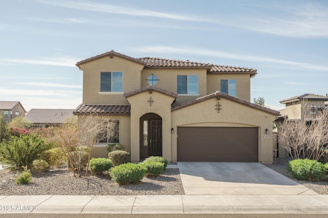 mediterranean / spanish house with a garage, driveway, a tiled roof, and stucco siding