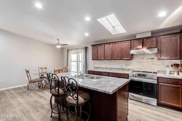 kitchen featuring under cabinet range hood, stainless steel electric stove, decorative backsplash, and a sink