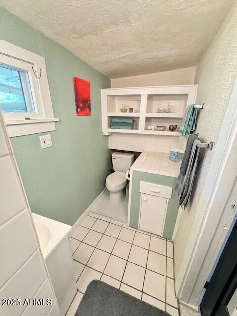bathroom featuring a textured wall, a textured ceiling, toilet, and tile patterned floors