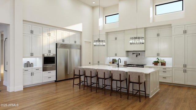 kitchen with appliances with stainless steel finishes, hanging light fixtures, an island with sink, white cabinets, and sink