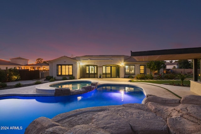 pool at dusk featuring an in ground hot tub and a patio