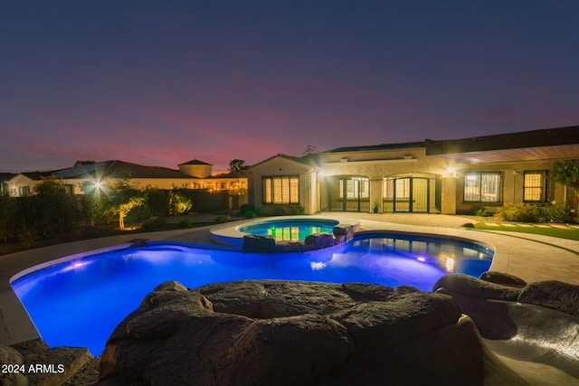 pool at dusk with a patio area and an in ground hot tub