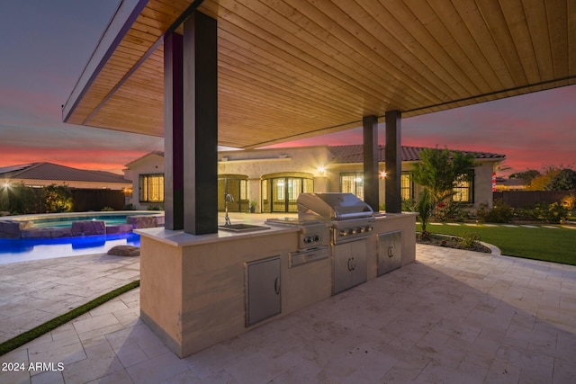 patio terrace at dusk with area for grilling, sink, grilling area, and a swimming pool with hot tub