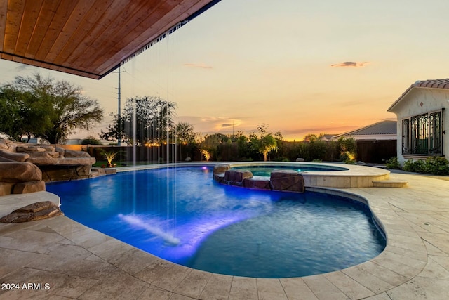 pool at dusk featuring pool water feature, a patio, and an in ground hot tub