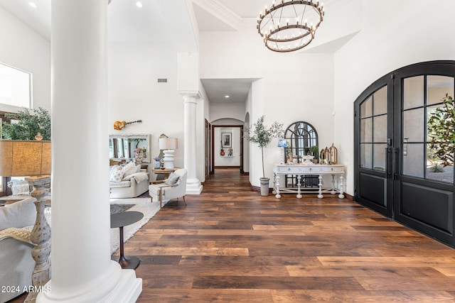 entrance foyer with french doors, a towering ceiling, ornate columns, a chandelier, and dark hardwood / wood-style floors