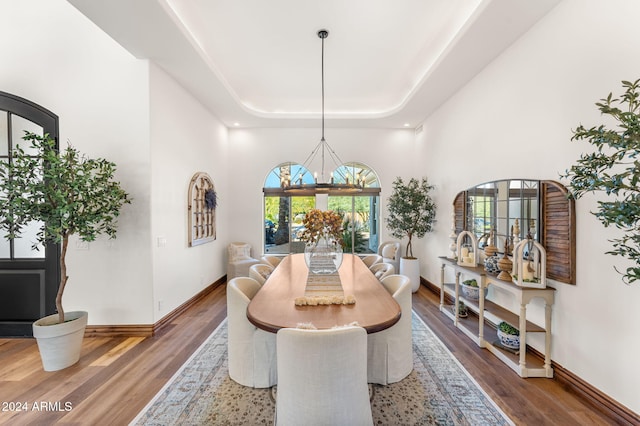 dining area with a raised ceiling, a towering ceiling, a chandelier, and hardwood / wood-style flooring