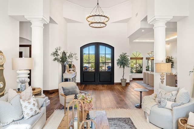 interior space featuring hardwood / wood-style floors, french doors, crown molding, a towering ceiling, and a notable chandelier