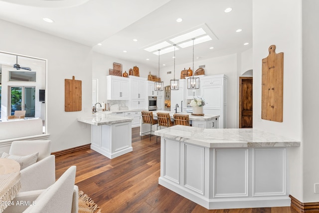 kitchen featuring ceiling fan, hanging light fixtures, dark hardwood / wood-style flooring, kitchen peninsula, and white cabinets