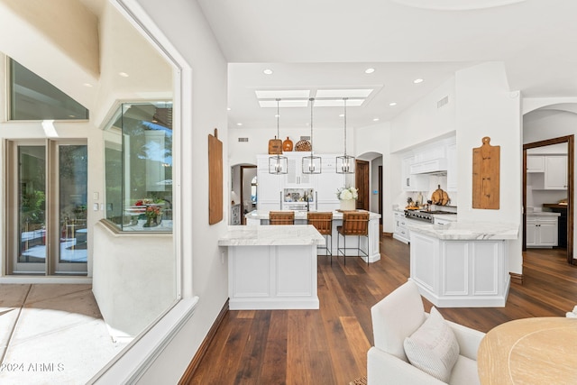 kitchen featuring light stone countertops, dark hardwood / wood-style flooring, kitchen peninsula, pendant lighting, and white cabinets