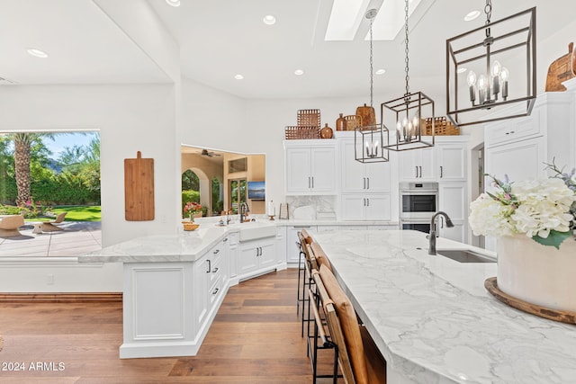 kitchen with kitchen peninsula, light stone countertops, sink, light hardwood / wood-style floors, and white cabinetry