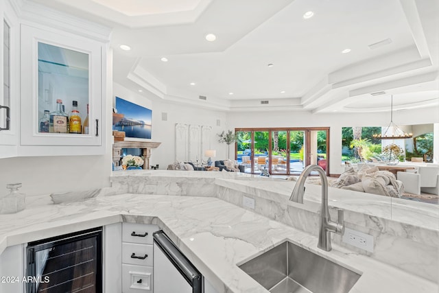 kitchen with a tray ceiling, beverage cooler, sink, an inviting chandelier, and white cabinetry