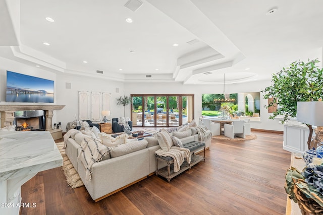 living room featuring a raised ceiling, a premium fireplace, wood-type flooring, and an inviting chandelier