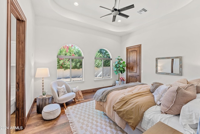 bedroom with ceiling fan, a raised ceiling, and light wood-type flooring