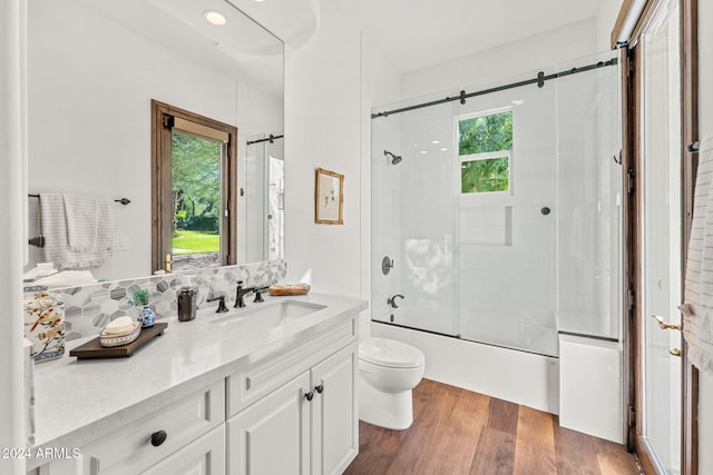 full bathroom with toilet, hardwood / wood-style floors, a healthy amount of sunlight, and bath / shower combo with glass door