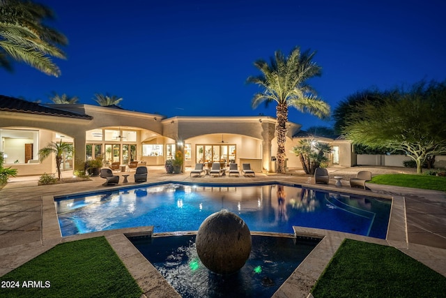 pool at night featuring a patio area