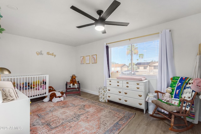 bedroom featuring dark hardwood / wood-style floors, a nursery area, and ceiling fan