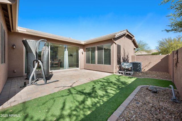 back of property with central AC, a fenced backyard, stucco siding, a lawn, and a patio