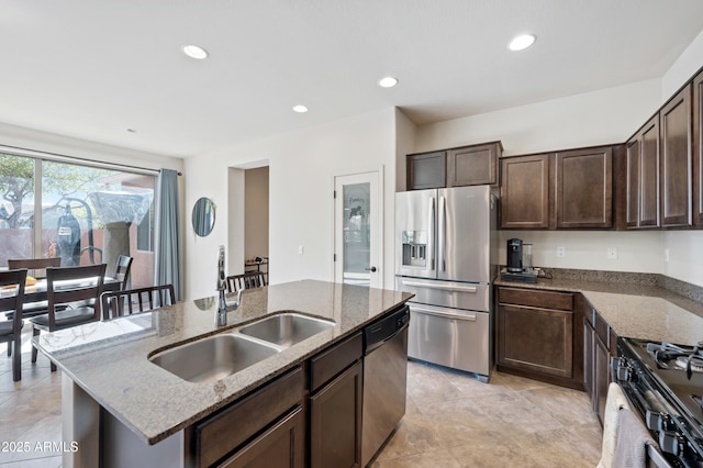 kitchen featuring dark stone counters, dark brown cabinetry, a kitchen island with sink, a sink, and stainless steel appliances