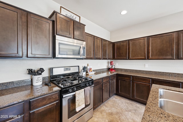 kitchen featuring light tile patterned floors, a sink, dark brown cabinets, dark stone counters, and stainless steel appliances