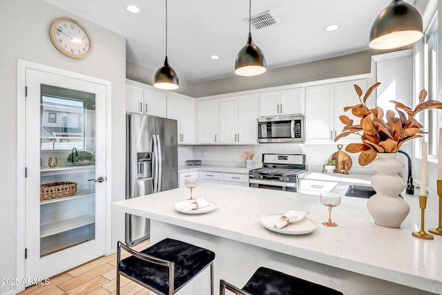 kitchen with visible vents, white cabinets, stainless steel appliances, a kitchen bar, and backsplash