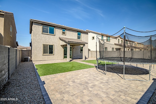 rear view of house with central AC unit, a trampoline, a fenced backyard, and stucco siding