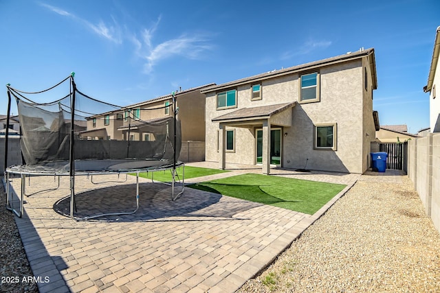 rear view of property with a patio area, a fenced backyard, a trampoline, and stucco siding