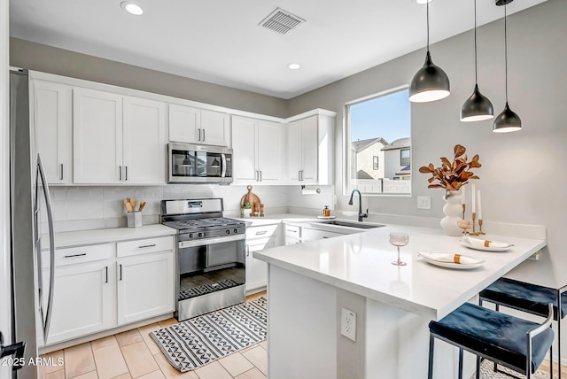 kitchen featuring visible vents, appliances with stainless steel finishes, white cabinets, a sink, and a peninsula