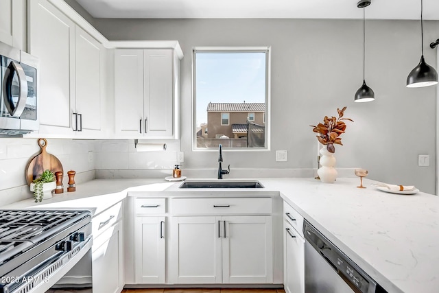 kitchen with stainless steel appliances, a sink, white cabinets, hanging light fixtures, and light stone countertops