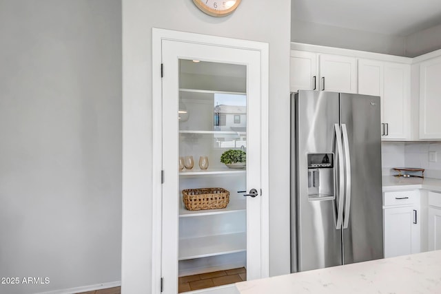 kitchen with stainless steel refrigerator with ice dispenser, white cabinetry, and light stone countertops