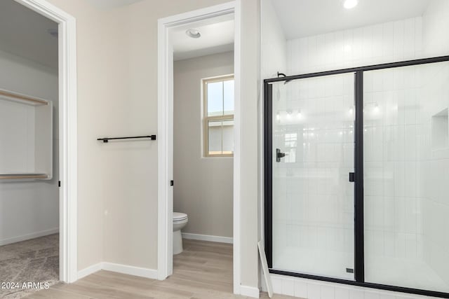 bathroom with hardwood / wood-style floors, toilet, and a shower with door