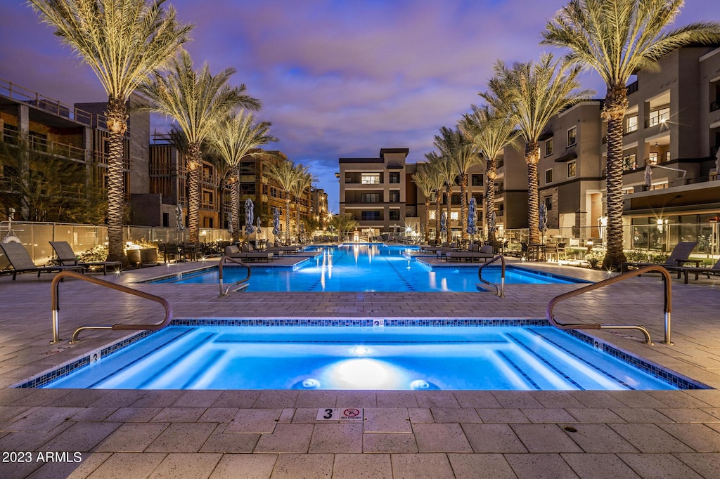 pool at dusk with a community hot tub and a patio area