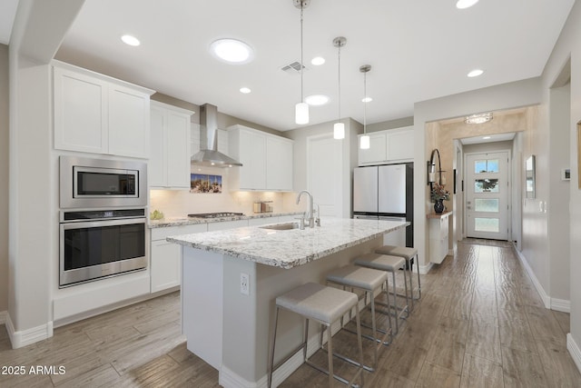 18746 W Rancho Dr, Litchfield Park, AZ 85340 - kitchen featuring a sink, visible vents, stainless steel appliances, wall chimney exhaust hood, and an island with sink