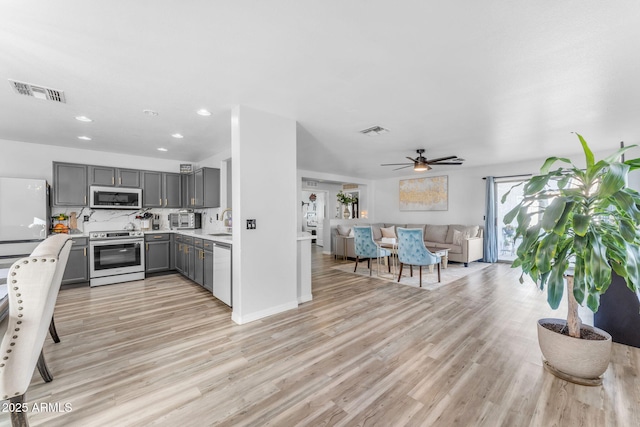 kitchen with light hardwood / wood-style floors, gray cabinets, ceiling fan, appliances with stainless steel finishes, and tasteful backsplash