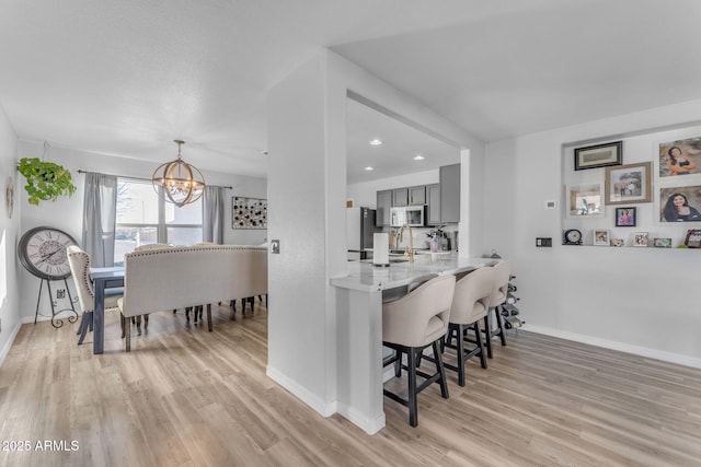 kitchen featuring a notable chandelier, a kitchen bar, light hardwood / wood-style flooring, gray cabinetry, and stainless steel fridge