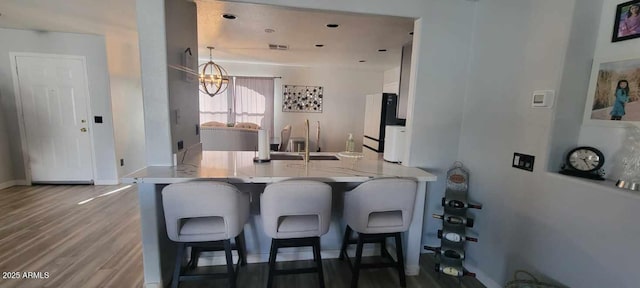 kitchen featuring kitchen peninsula, black refrigerator, a notable chandelier, a kitchen breakfast bar, and white cabinets