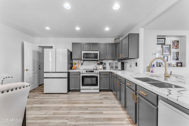 kitchen featuring gray cabinets, appliances with stainless steel finishes, tasteful backsplash, light stone countertops, and sink