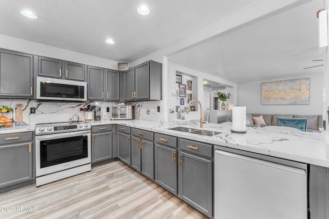 kitchen featuring gray cabinets, kitchen peninsula, decorative backsplash, sink, and appliances with stainless steel finishes