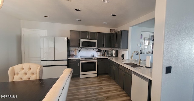 kitchen with backsplash, sink, white appliances, dark wood-type flooring, and light stone counters