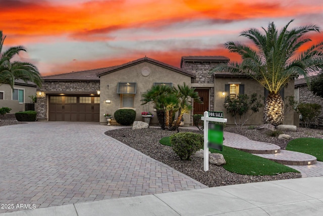 view of front of property featuring decorative driveway, stone siding, an attached garage, and stucco siding