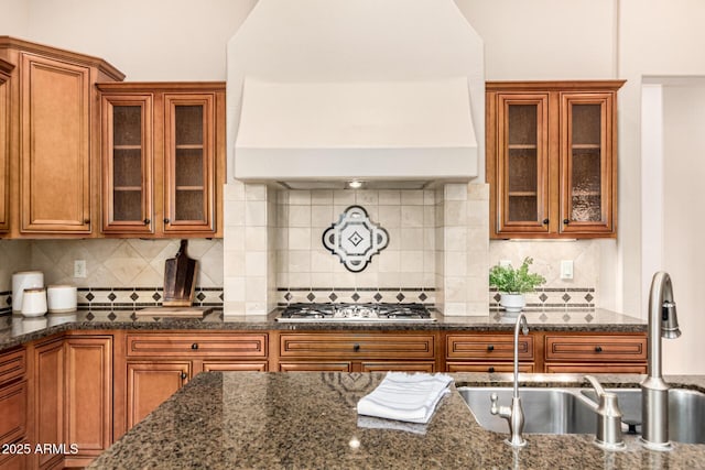 28247 N 128th Dr, Peoria, AZ 85383 - kitchen featuring custom exhaust hood, stainless steel gas stovetop, brown cabinetry, a sink, and dark stone countertops