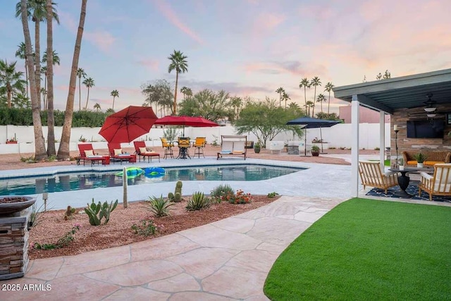 pool at dusk with a patio and ceiling fan