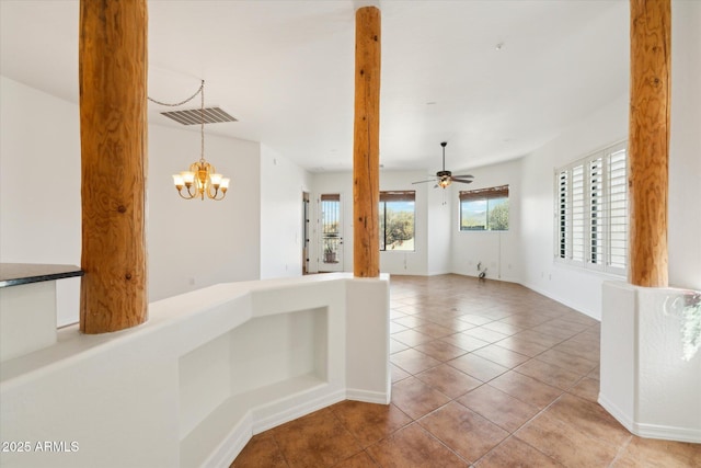 empty room featuring tile patterned floors, visible vents, baseboards, and ceiling fan with notable chandelier