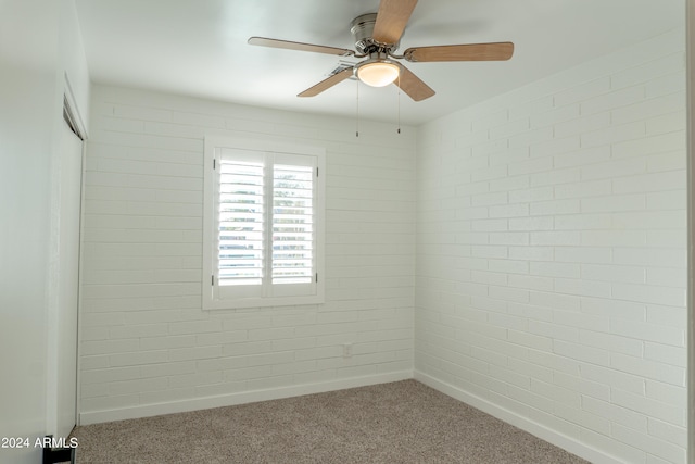 carpeted empty room with brick wall and ceiling fan